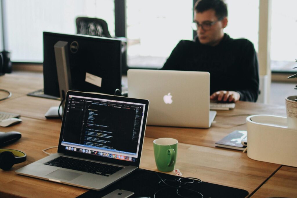 Man in Black Shirt Sits Behind Desk With Computers